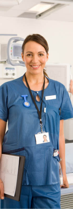 A vertical shot of a young adult radiologist holding a clipboard while smiling at the camera in a radiology department with her colleague working in the background