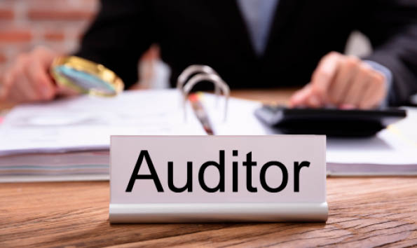 Nameplate With Auditor Title Kept On Desk In Front Of Businessman Examining The Invoices