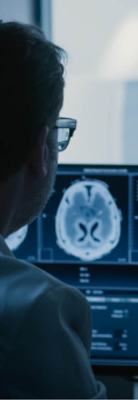 In Control Room Doctor and Radiologist Discuss Diagnosis while Watching Procedure and Monitors Showing Brain Scans Results, In the Background Patient Undergoes MRI or CT Scan Procedure.