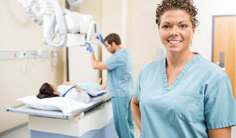 Portrait of radiologist smiling while colleague preparing patient for xray in examination room