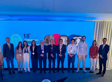 Dez adultos em p em um palco com fundo azul exibindo o texto 18º Congresso e s mbolos relacionados, todos usando crach s e vestidos com roupas formais e casuais.  Descri  o gerada por IA